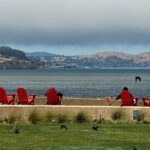 Red Adirondack Chairs line up cliffside for a panoramic view of the bay.